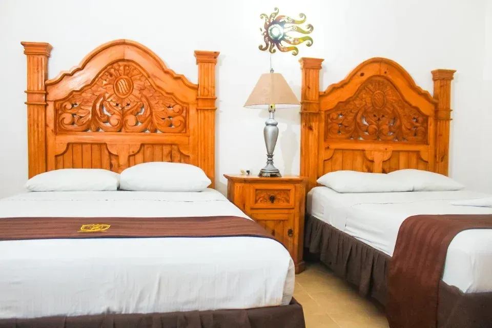 Dos camas con cabeceros de madera tallados de forma ornamentada en una habitación con una mesita de noche .
