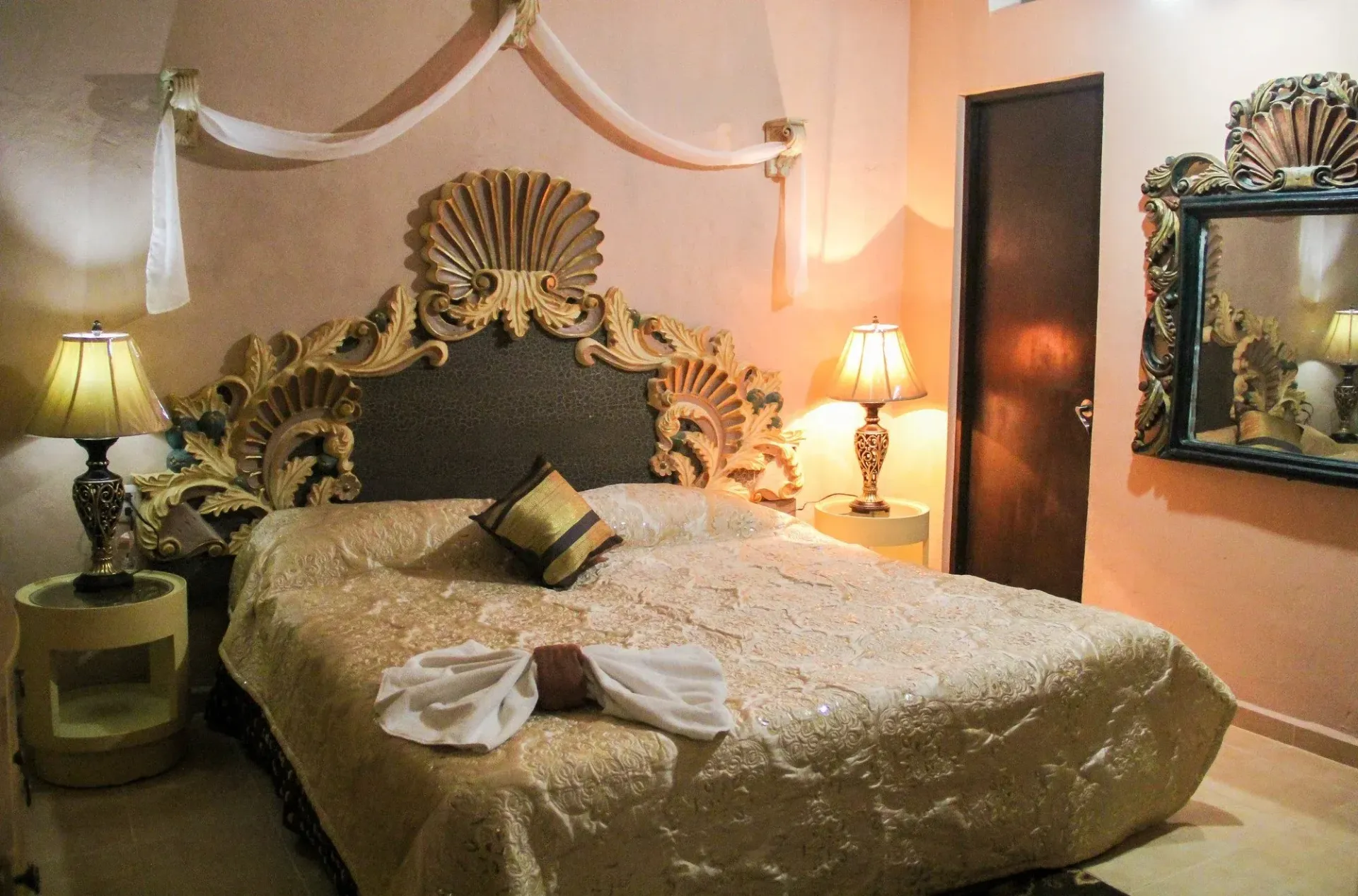 Luxurious bedroom with ornate gold headboard, lamps, mirror, and a gold bedspread.