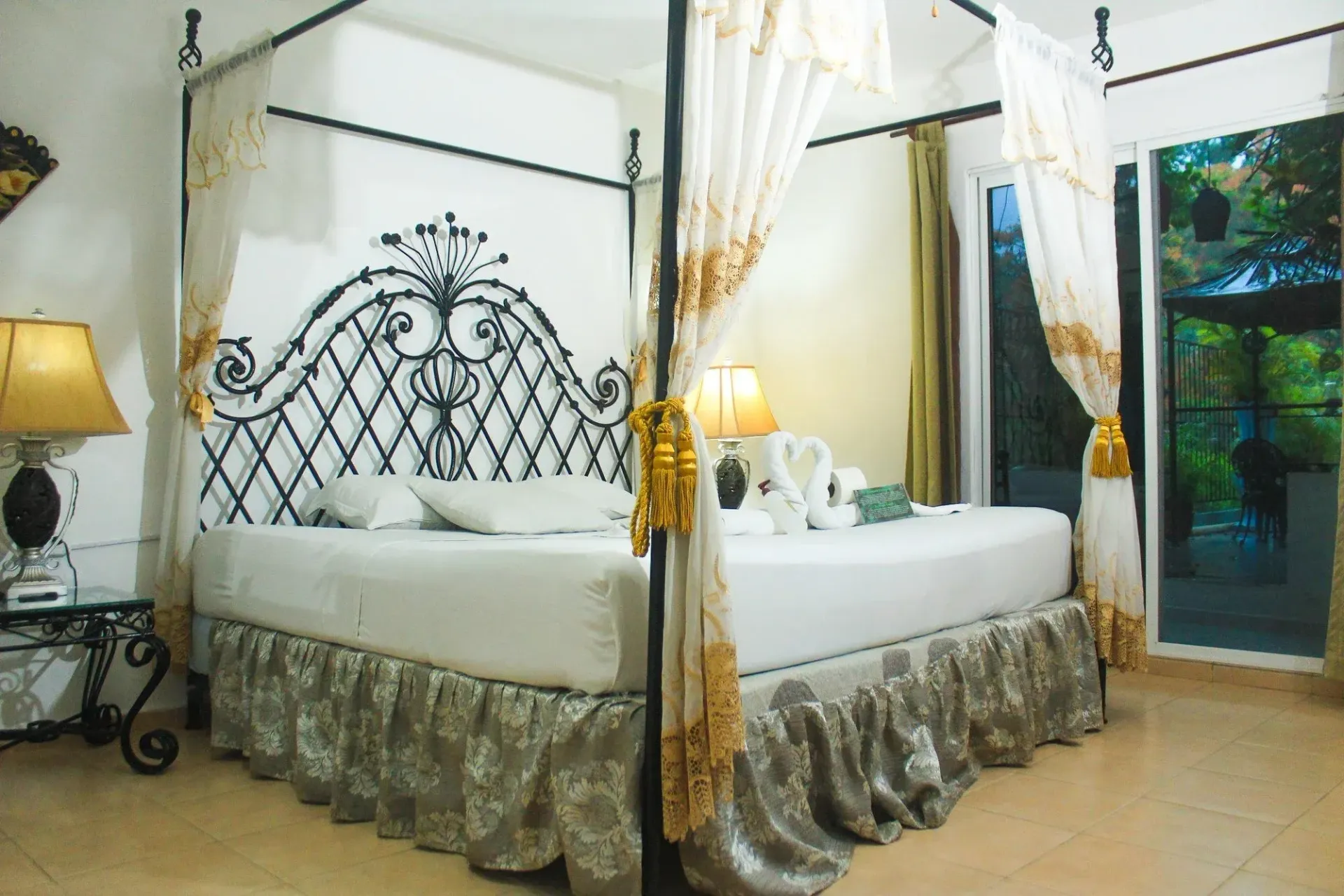 Elegante dormitorio con cama con dosel, cabecera ornamentada, cortinas blancas y doradas y vista.