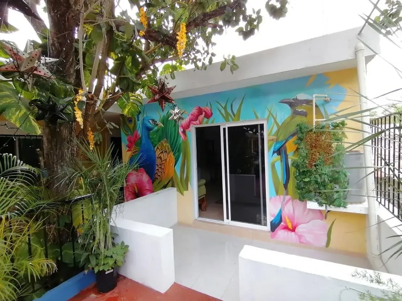 Exterior view of a building with a mural of colorful birds and flowers; trees and plants are also present.