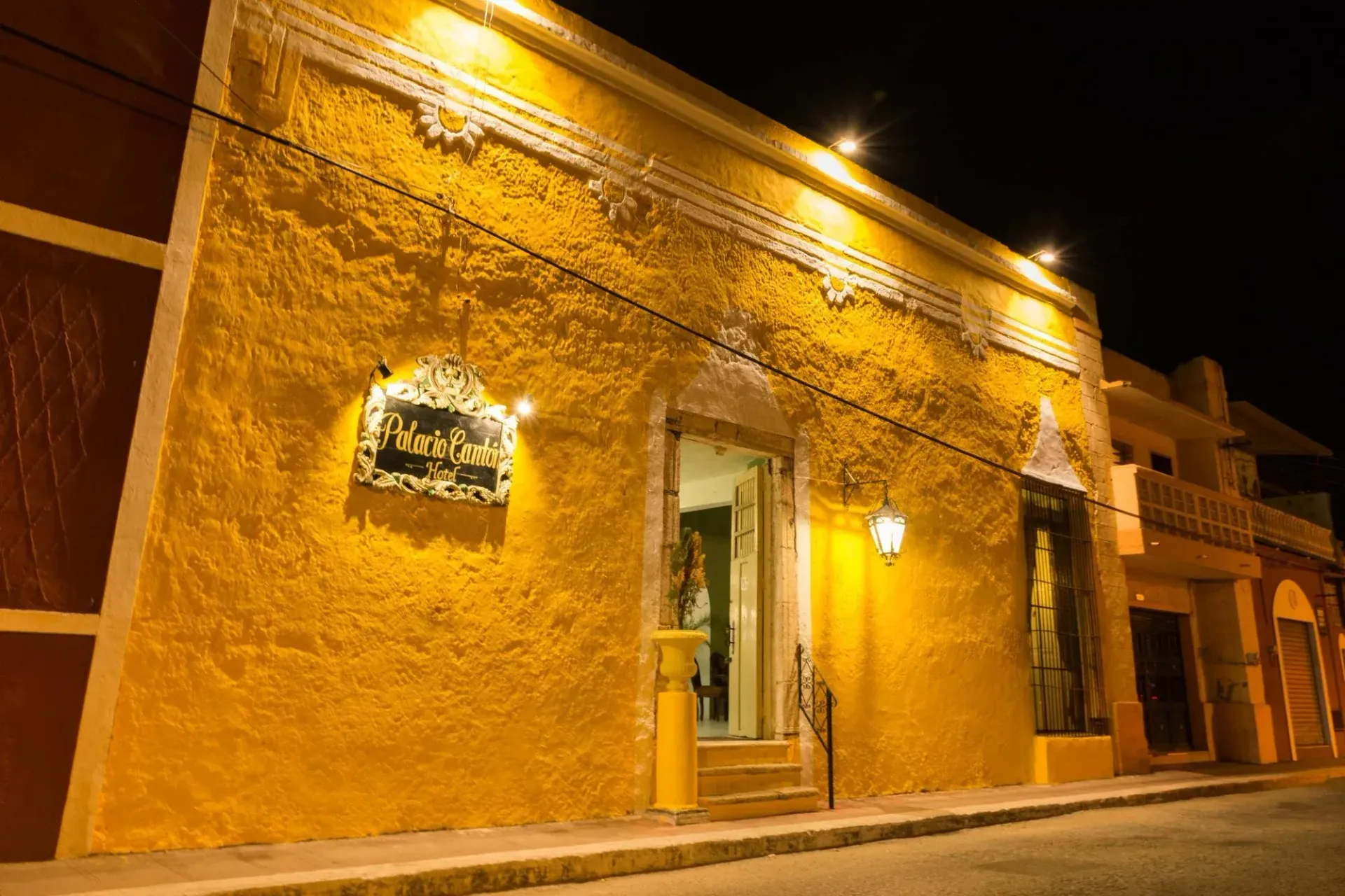 Yellow stucco building at night, with illuminated entrance and sign.