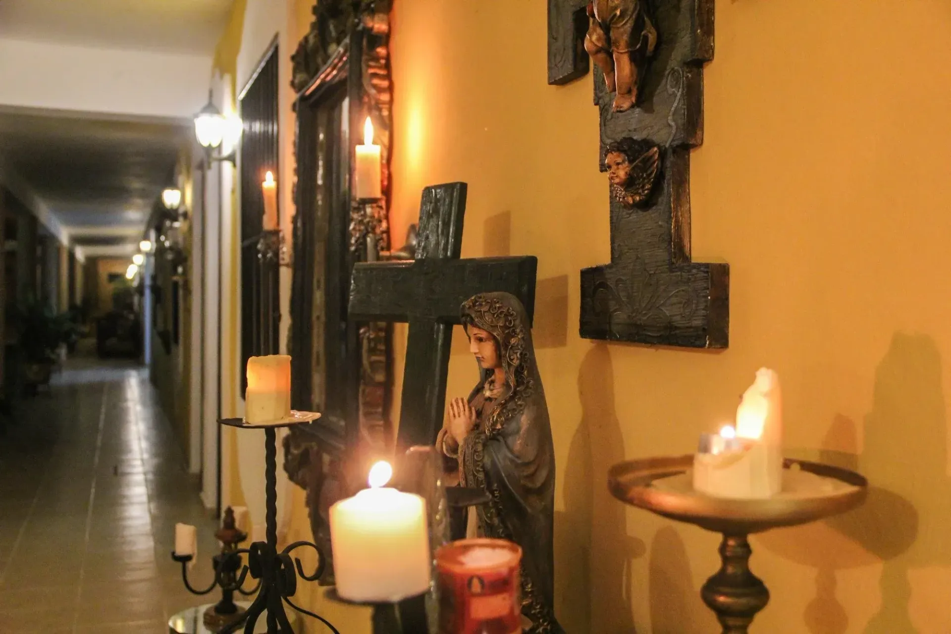 Hallway with religious statues, lit candles, and cross decorations.