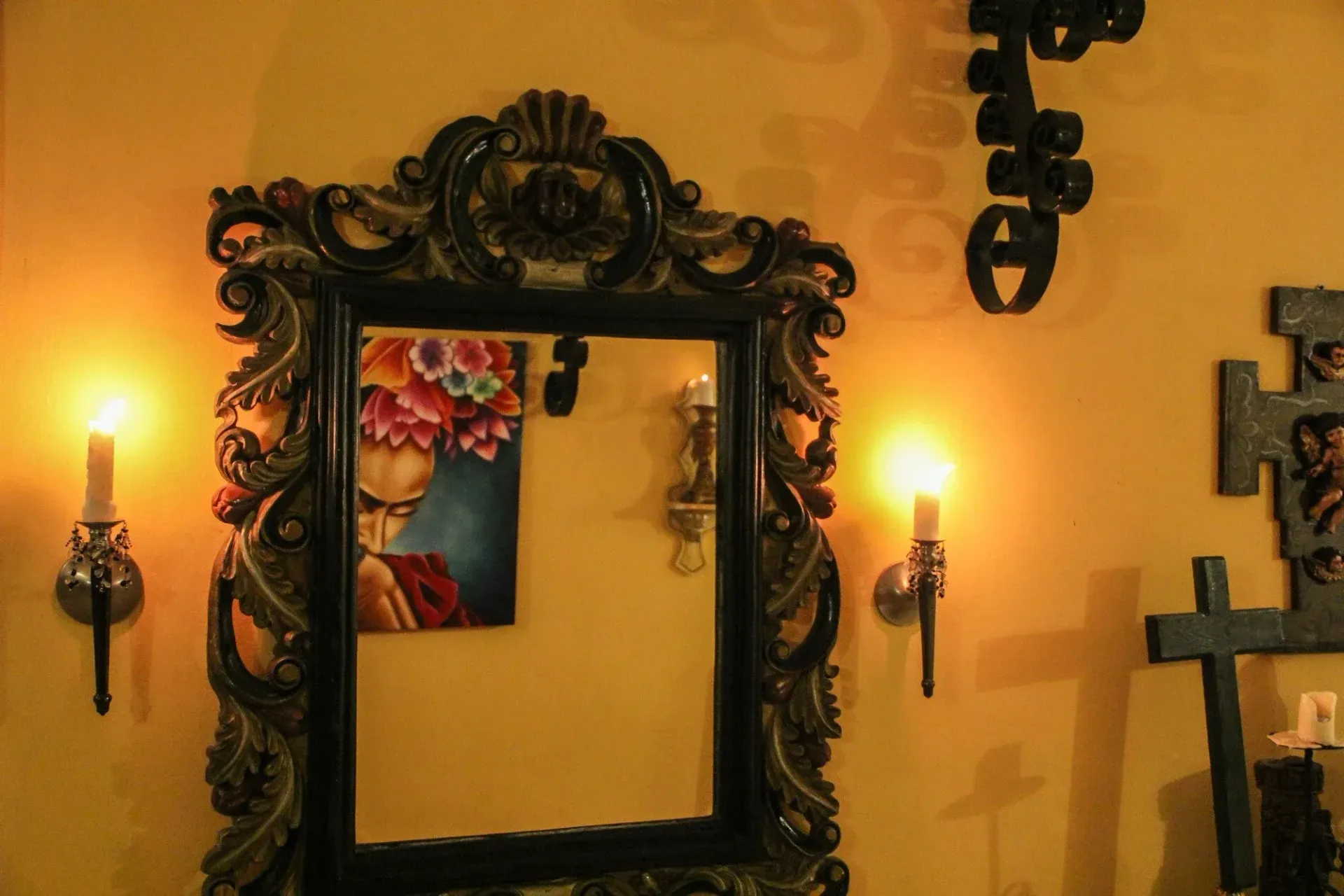 Ornate mirror with painting reflection, flanked by lit sconce candles on yellow wall.