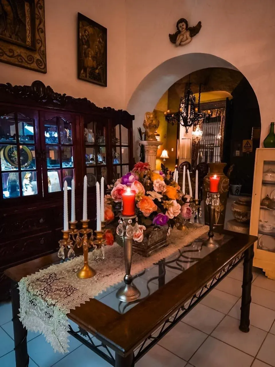 Antique dining table set for a celebration, with flowers, candles, and a decorated china cabinet.