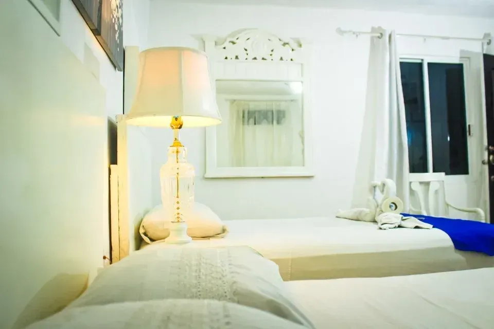 White bedroom with two beds, a lamp, and a mirror.