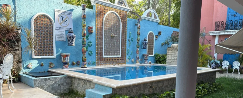 A blue wall with a small pool, decorated with tiles and pots, in an outdoor setting.