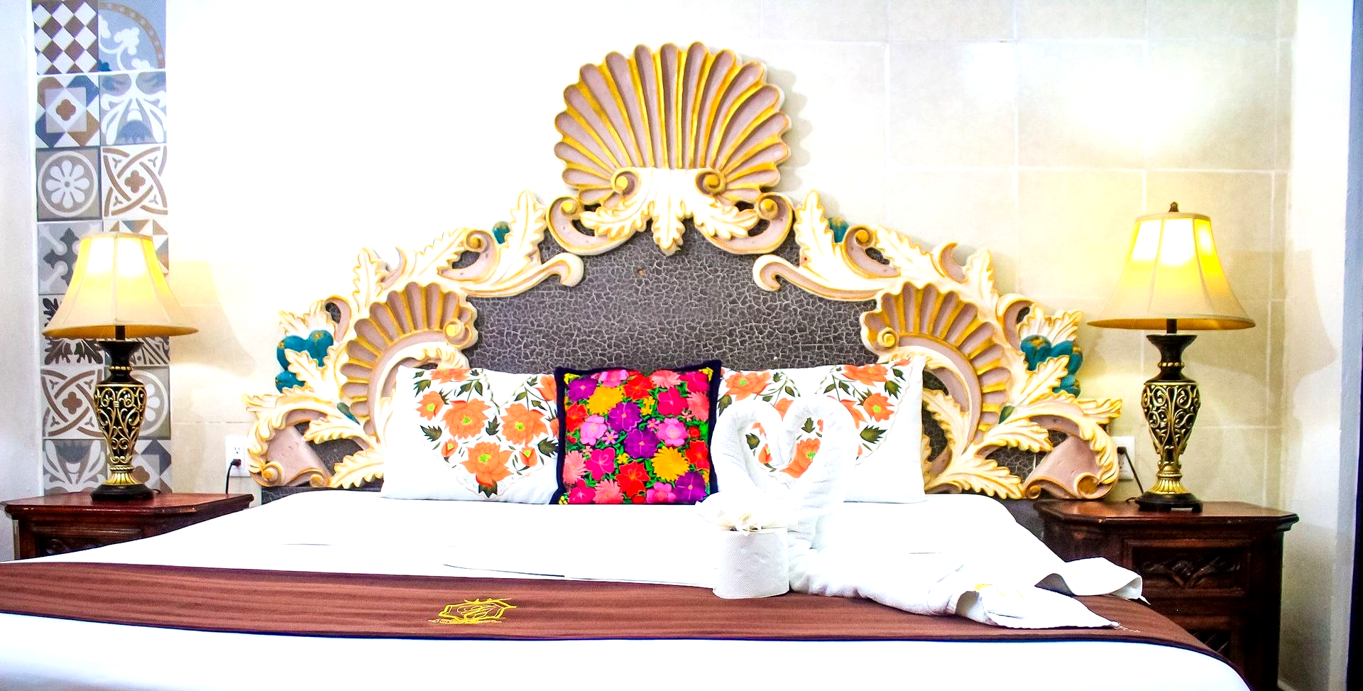 Dormitorio adornado con una cabecera grande, lámparas de noche y almohadas decorativas en la cama.