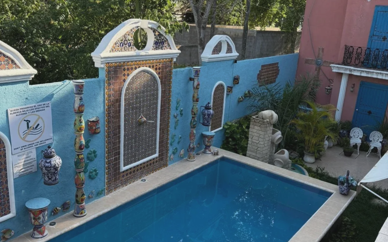 Blue-tiled pool in an outdoor courtyard with decorative walls, arches, and a pink building.