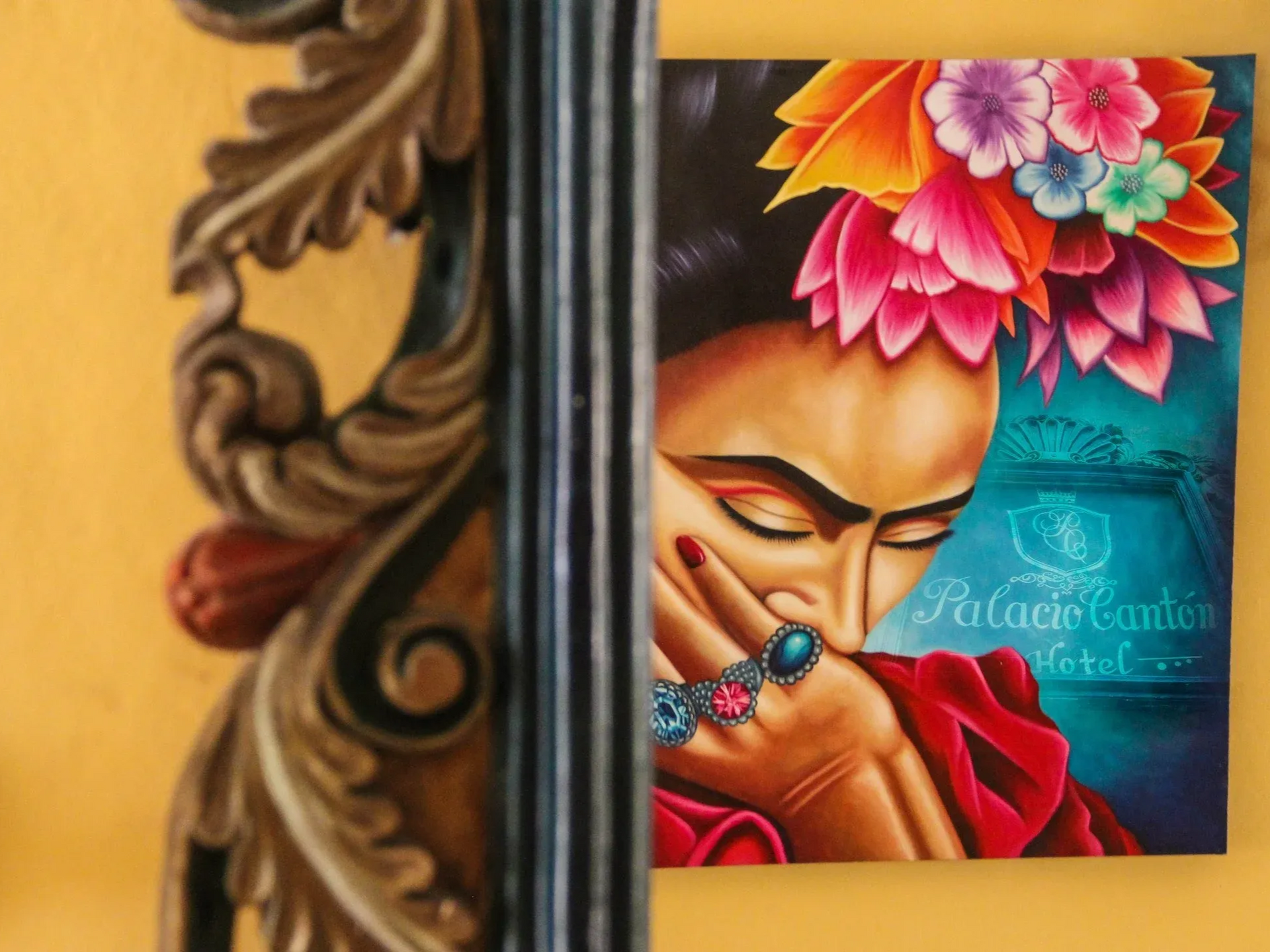 Painting of woman with flowers in hair, hand to face, colorful; beside ornate wooden frame.