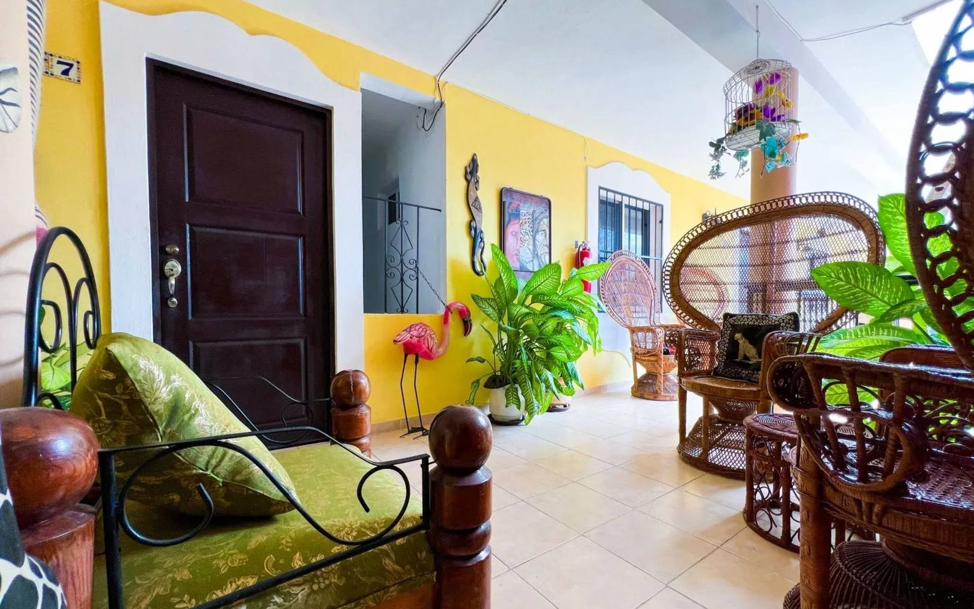 Yellow veranda with dark brown door, wicker furniture, and potted plants.