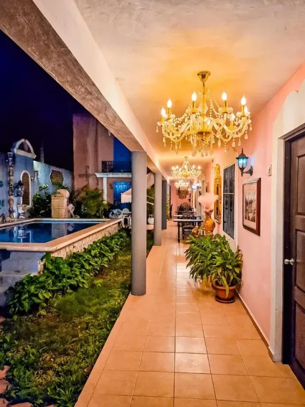 Pasillo largo con paredes rosas, candelabros y vista a una piscina por la noche.
