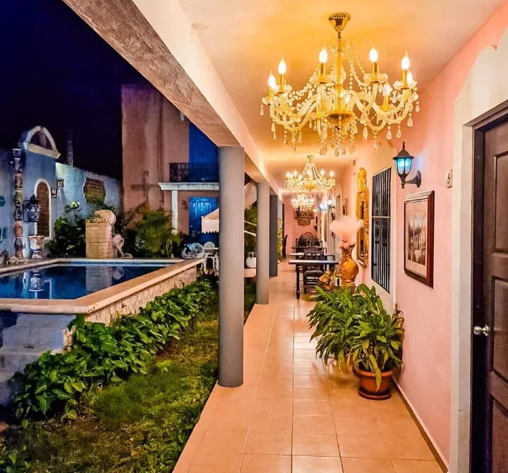 Long covered walkway with pool. Pink walls, chandeliers, potted plants, and doorway.