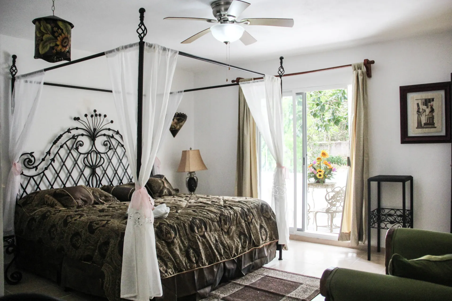 Dormitorio con cama con dosel, puerta corrediza al patio, edredón estampado, lámpara, ventilador de techo.