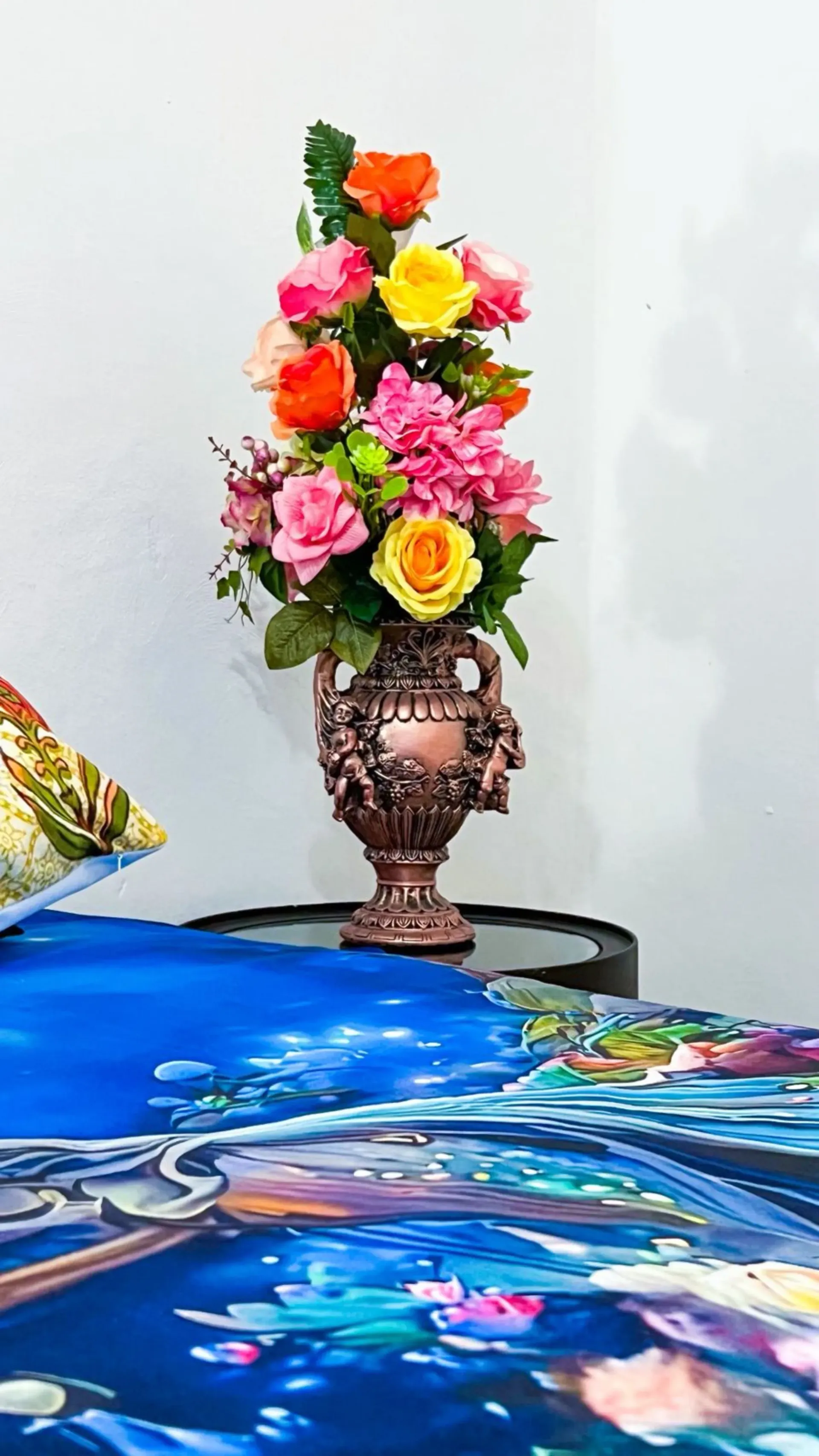 Un jarrón con flores de colores sobre una superficie oscura, contra una pared blanca.