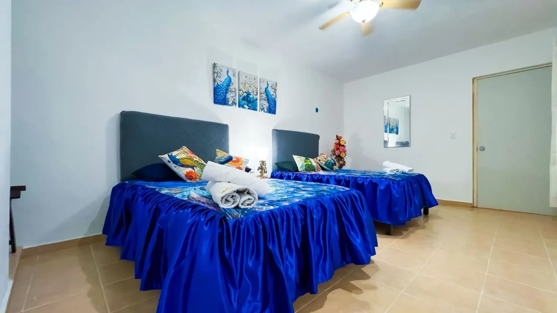 Dos camas individuales en una habitación con colchas azules, paredes blancas y obras de arte.