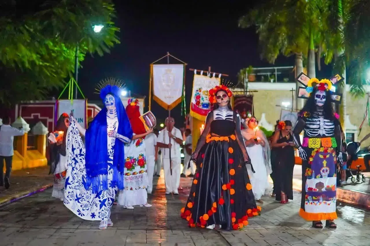 A nighttime parade of costumed figures, including skeleton-faced individuals, in colorful clothing and headdresses
