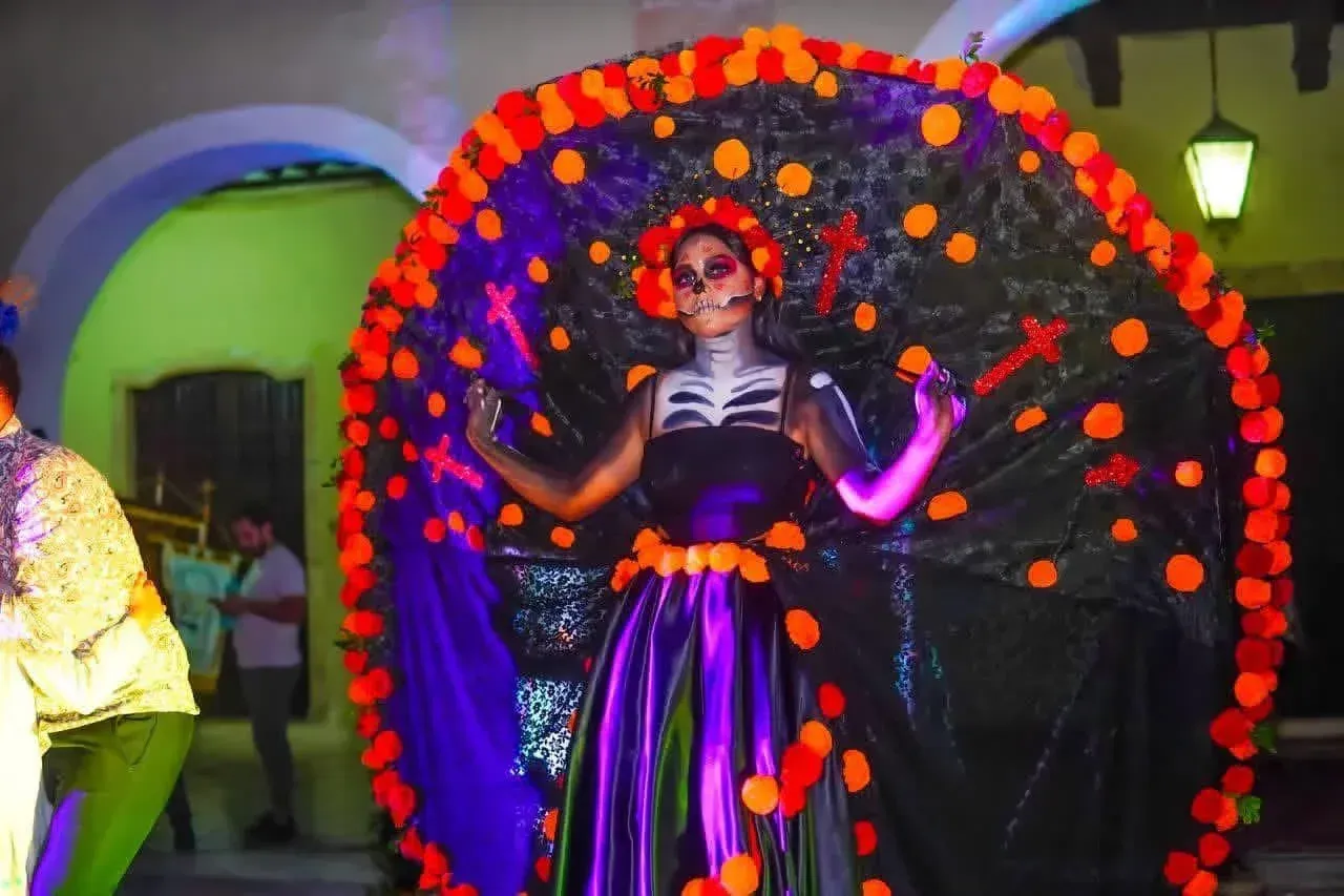 Woman in Día de los Muertos costume with skeleton face paint and a large, colorful headdress.