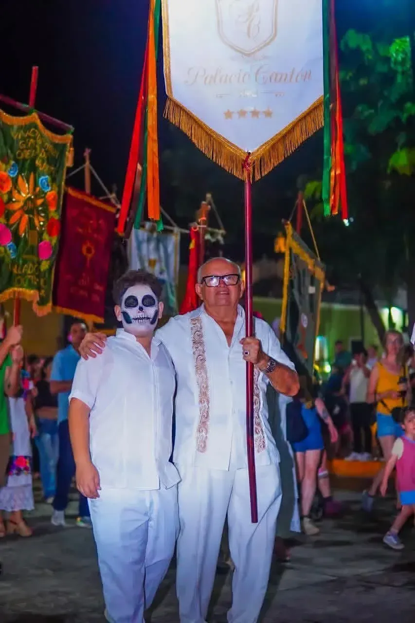 Two people in white outfits with a banner at a night parade. One has painted face.