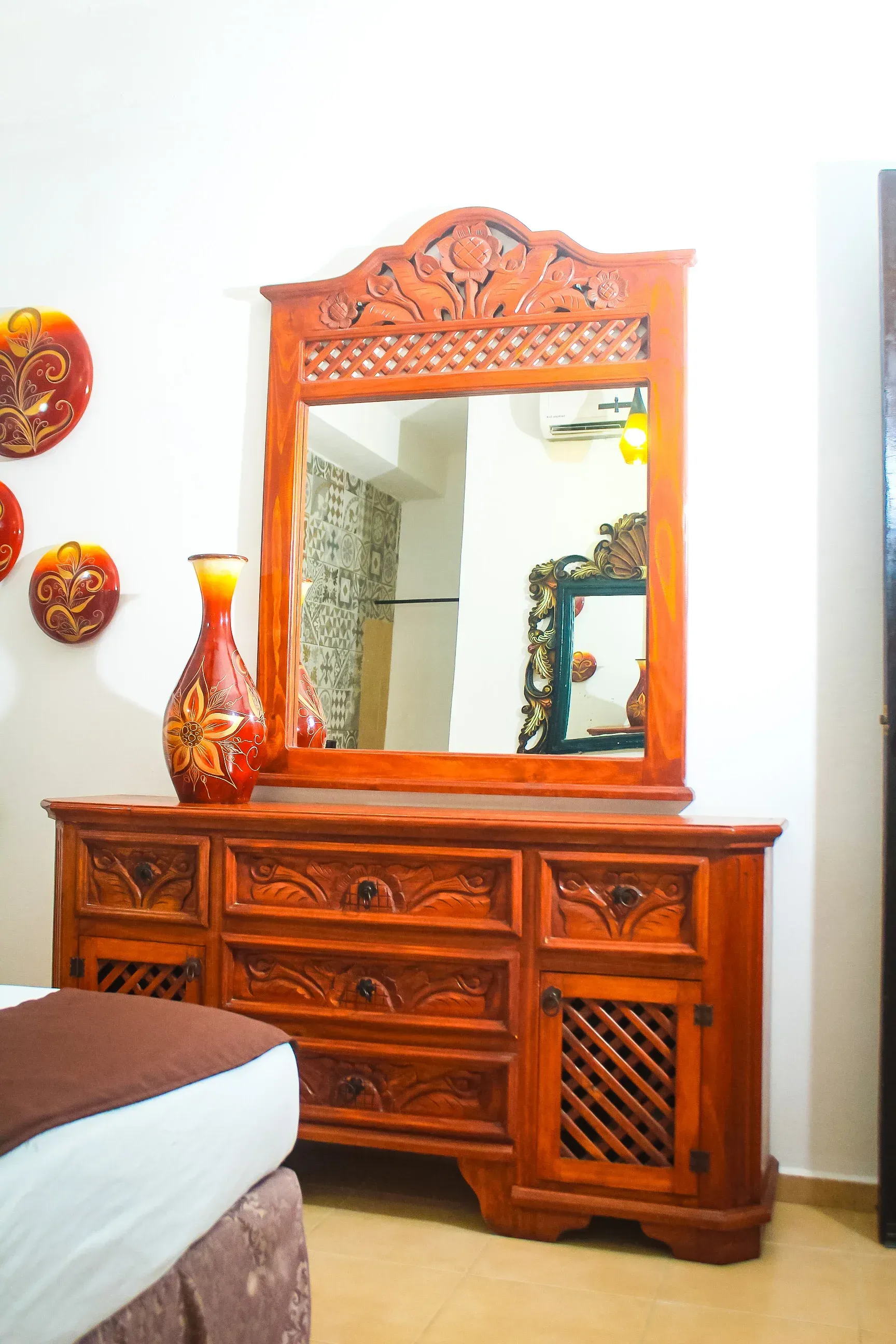 Cómoda de madera con espejo, jarrón y arte de pared en un dormitorio.