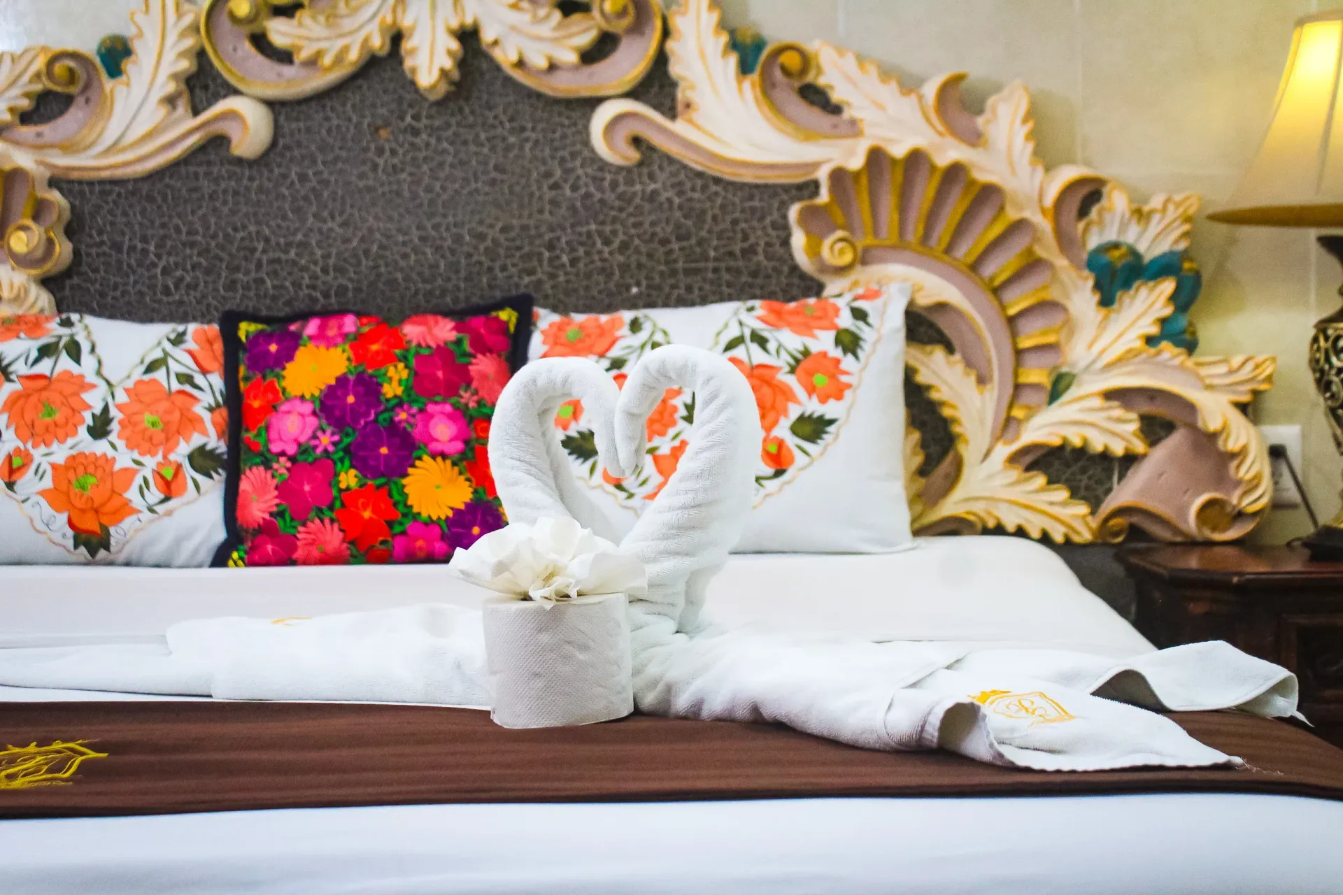 Cama con cabecero ornamentado, almohadas de colores y cisnes de toalla.