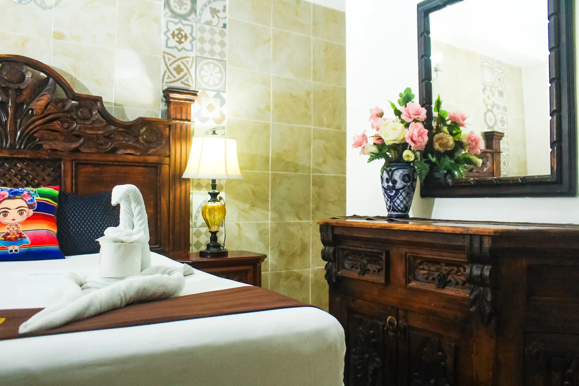 Dormitorio con cabecero de madera tallada, lámpara, jarrón con flores y cómoda.