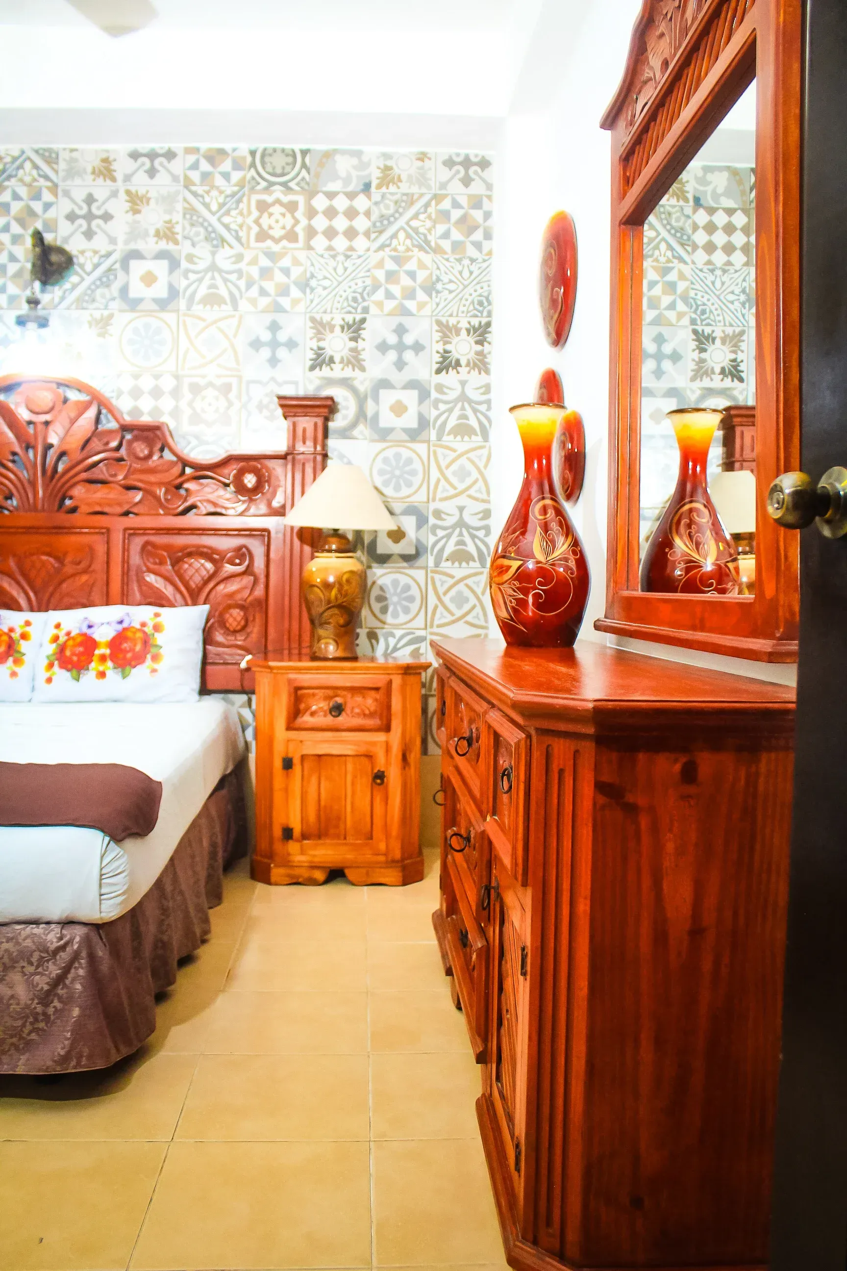 Dormitorio de madera con marco de cama tallado, tocador y pared de azulejos estampados.
