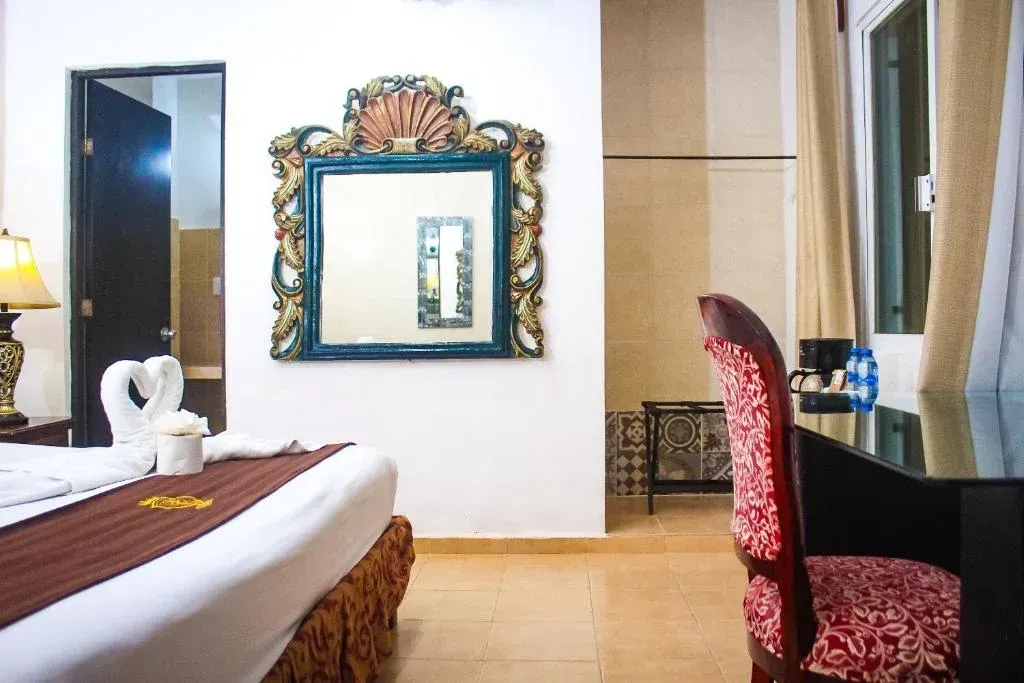 Interior de habitación de hotel con un gran espejo ornamentado, un escritorio y una cama.