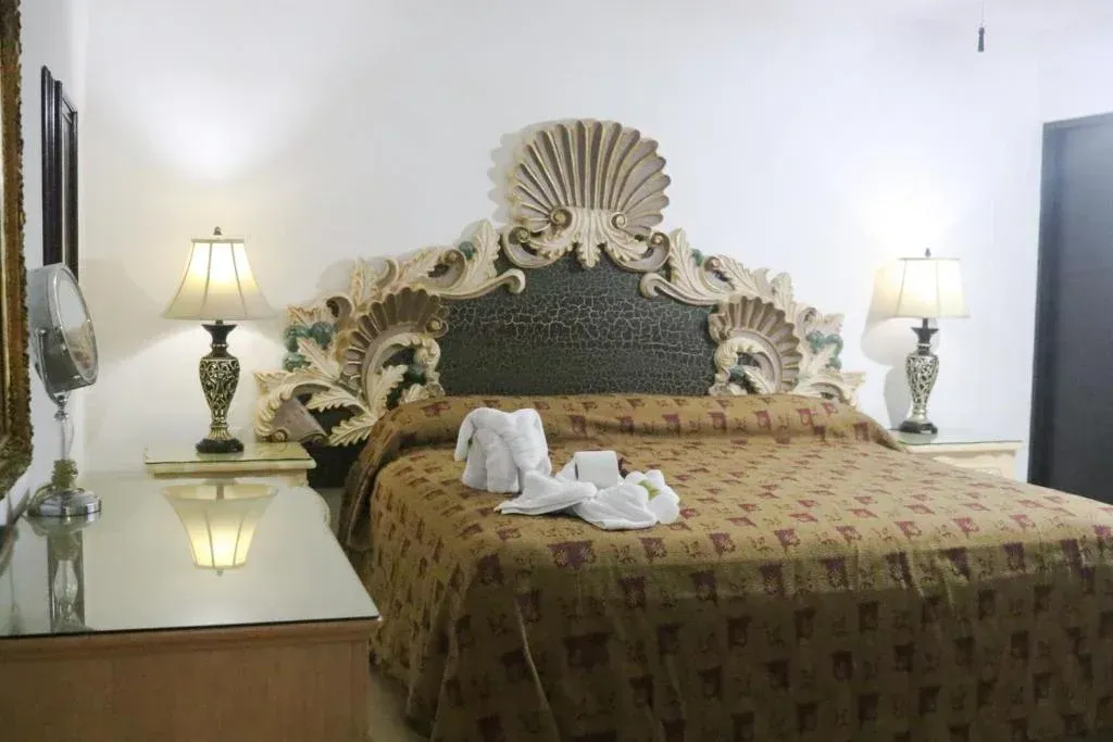 Dormitorio con un gran cabecero ornamentado, mesitas de noche con lámparas y una colcha estampada.