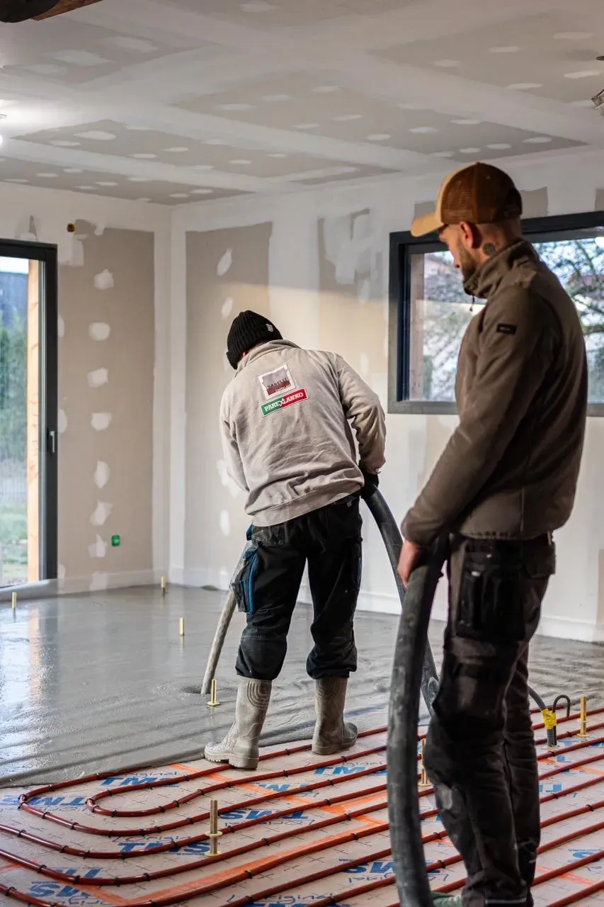 deux hommes travaillent sur un plancher chauffant dans une pièce.