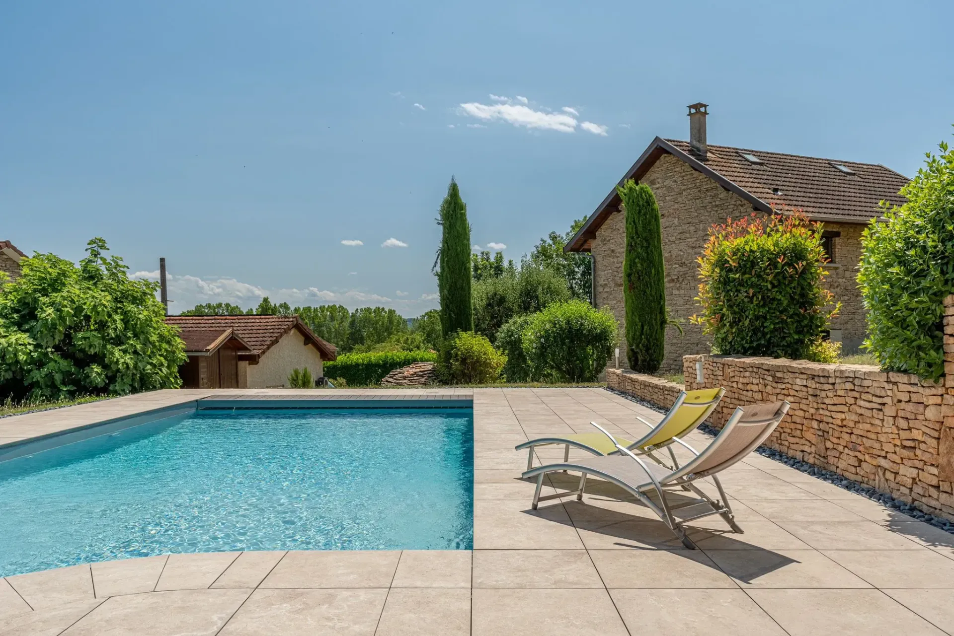 une grande piscine est entourée de transats et d'un mur en pierre.