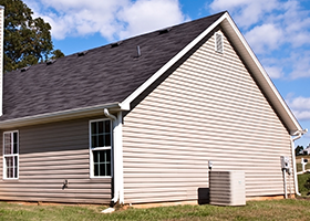 A house with a black roof and white siding is sitting on top of a lush green field.