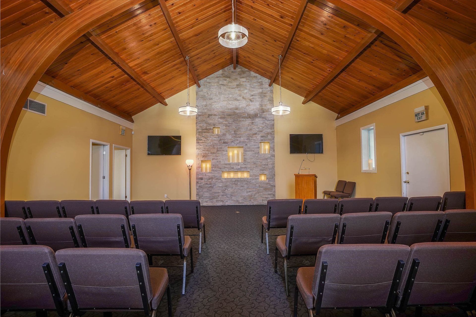 Empty chapel interior with rows of purple chairs, a stone fireplace, and a wooden vaulted ceiling
