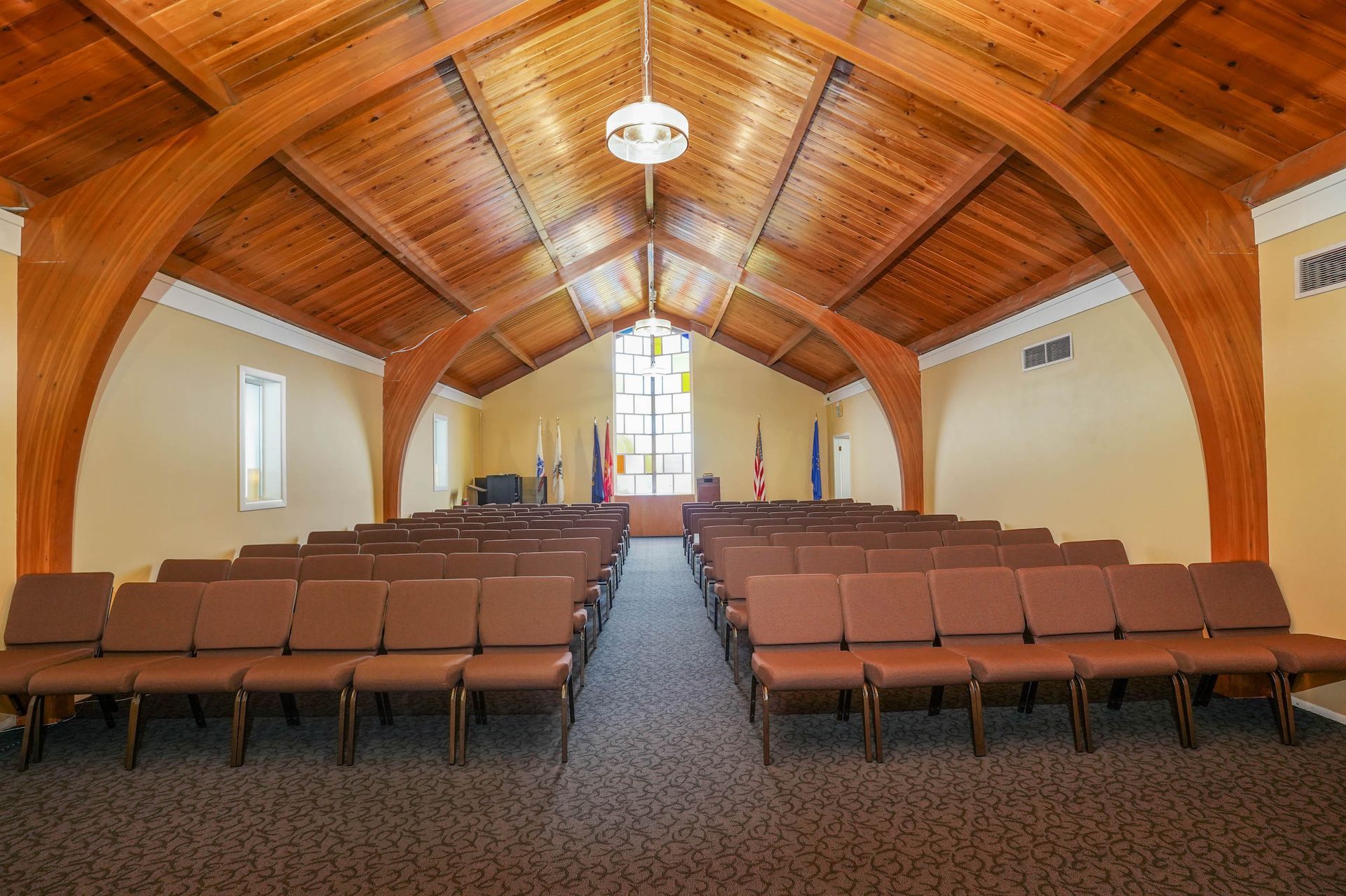 Empty chapel interior with wooden arched ceiling and rows of brown chairs facing the front