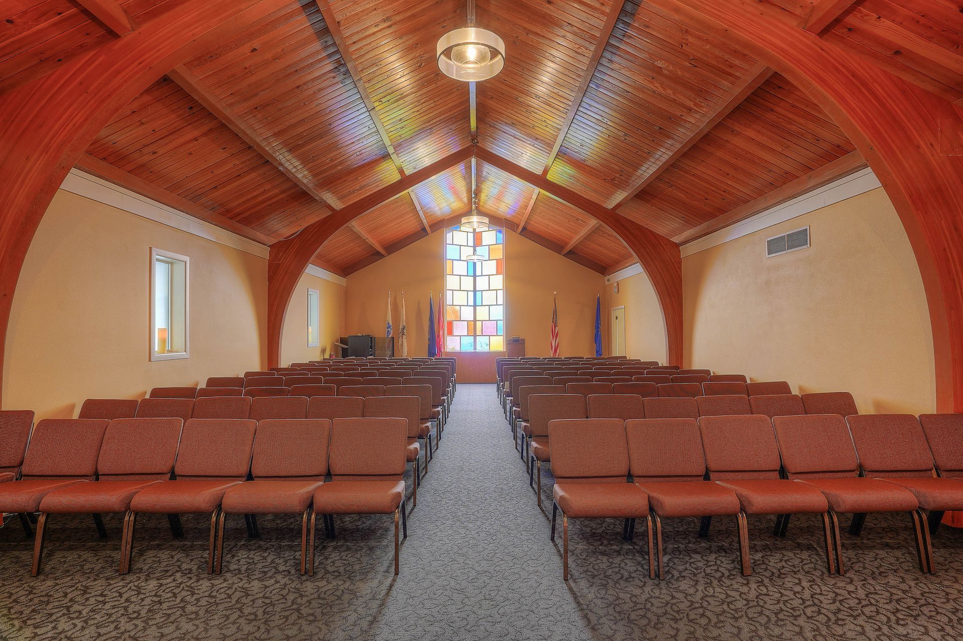 Empty church sanctuary with rows of wooden pews, a central aisle, and a stained-glass window at the front