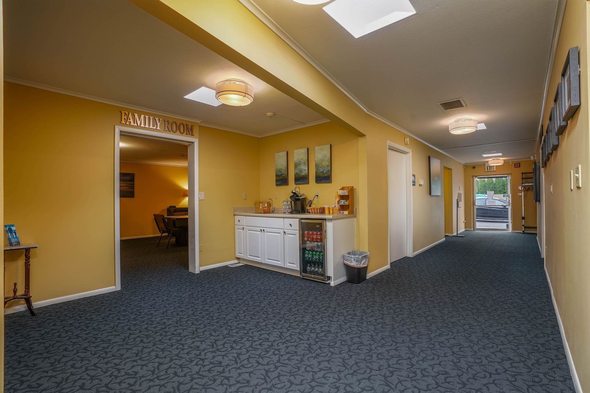 Empty office hallway with carpet, wall lights, and a reception area on the left