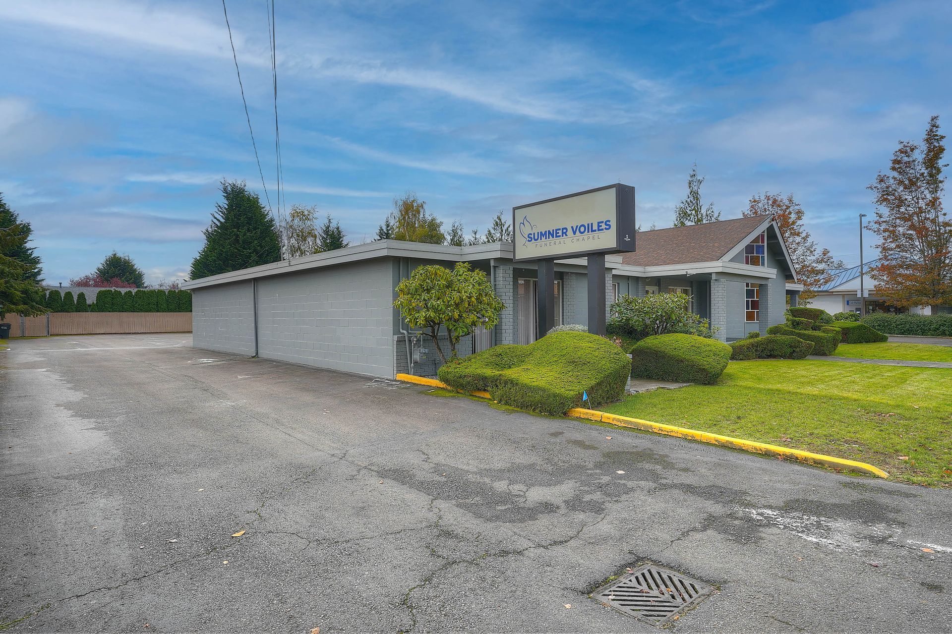 Small commercial building with gray stucco walls, parking lot, and trimmed bushes under a cloudy sky
