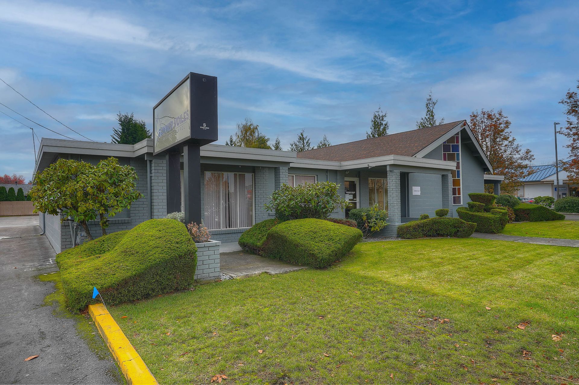 Suburban house with gray exterior, manicured lawn, and trimmed bushes under a blue sky