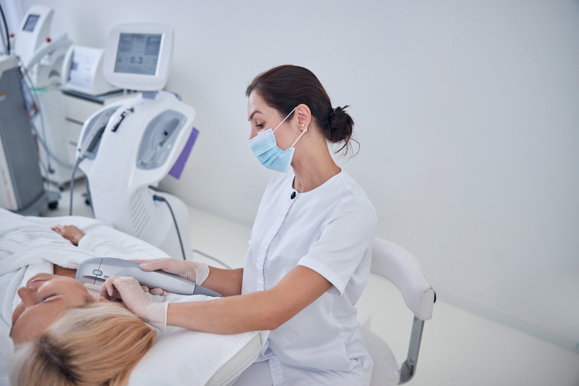 Nurse in white uniform and mask performing an ultrasound on a patient in a clinic room