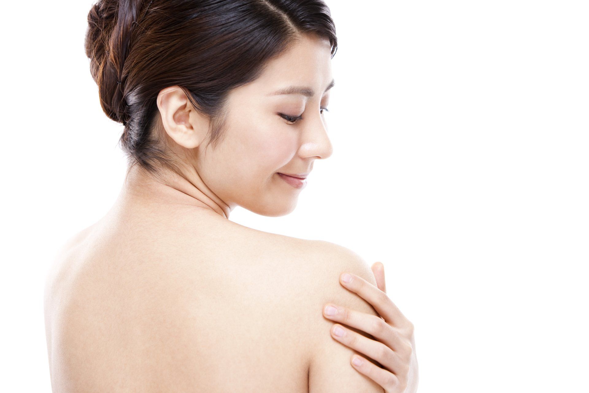Woman with bare shoulders smiling and touching her back on a white background