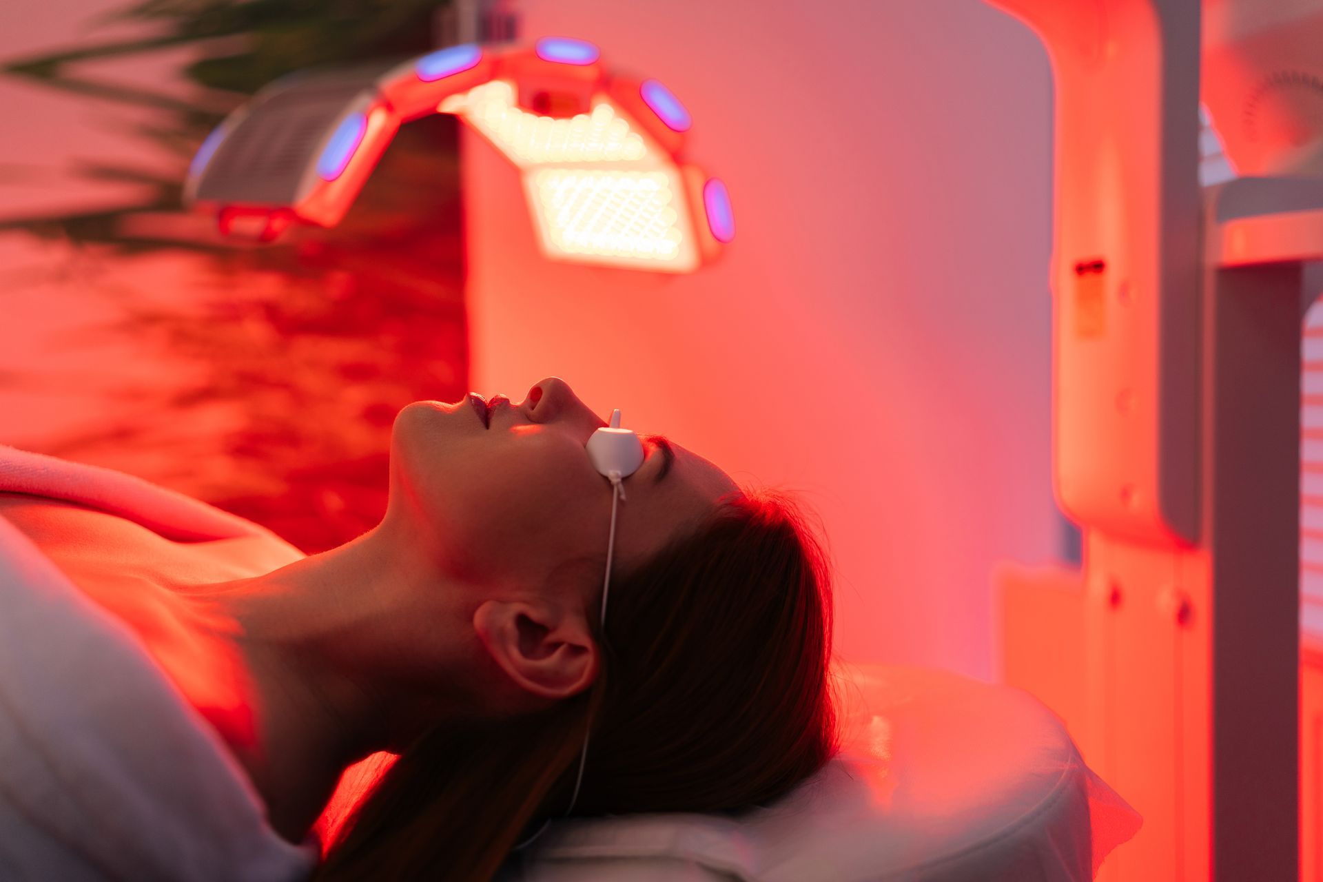 Person lying under a red light therapy panel with eye protection on, resting on a bed