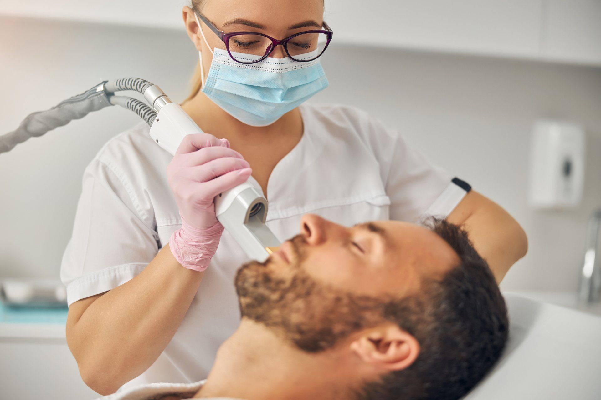 Dentist using a handheld scanner on a reclining patient in a clinic, both wearing masks and gloves
