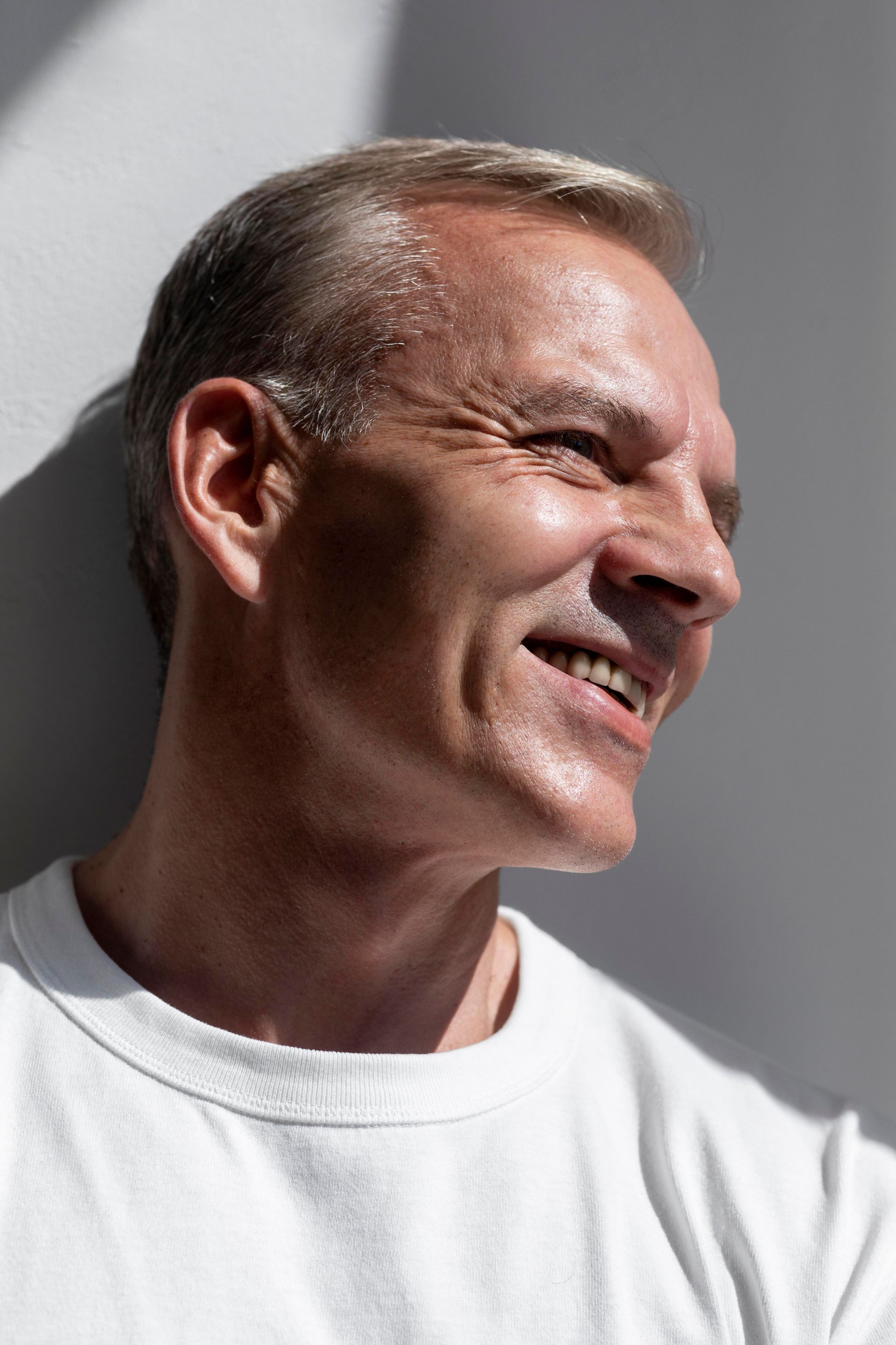 Smiling man in a white shirt against a gray background, shown in profile.
