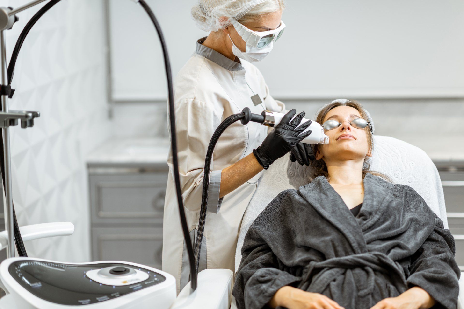 Aesthetic treatment in a clinic as a practitioner applies a facial device to a reclining patient