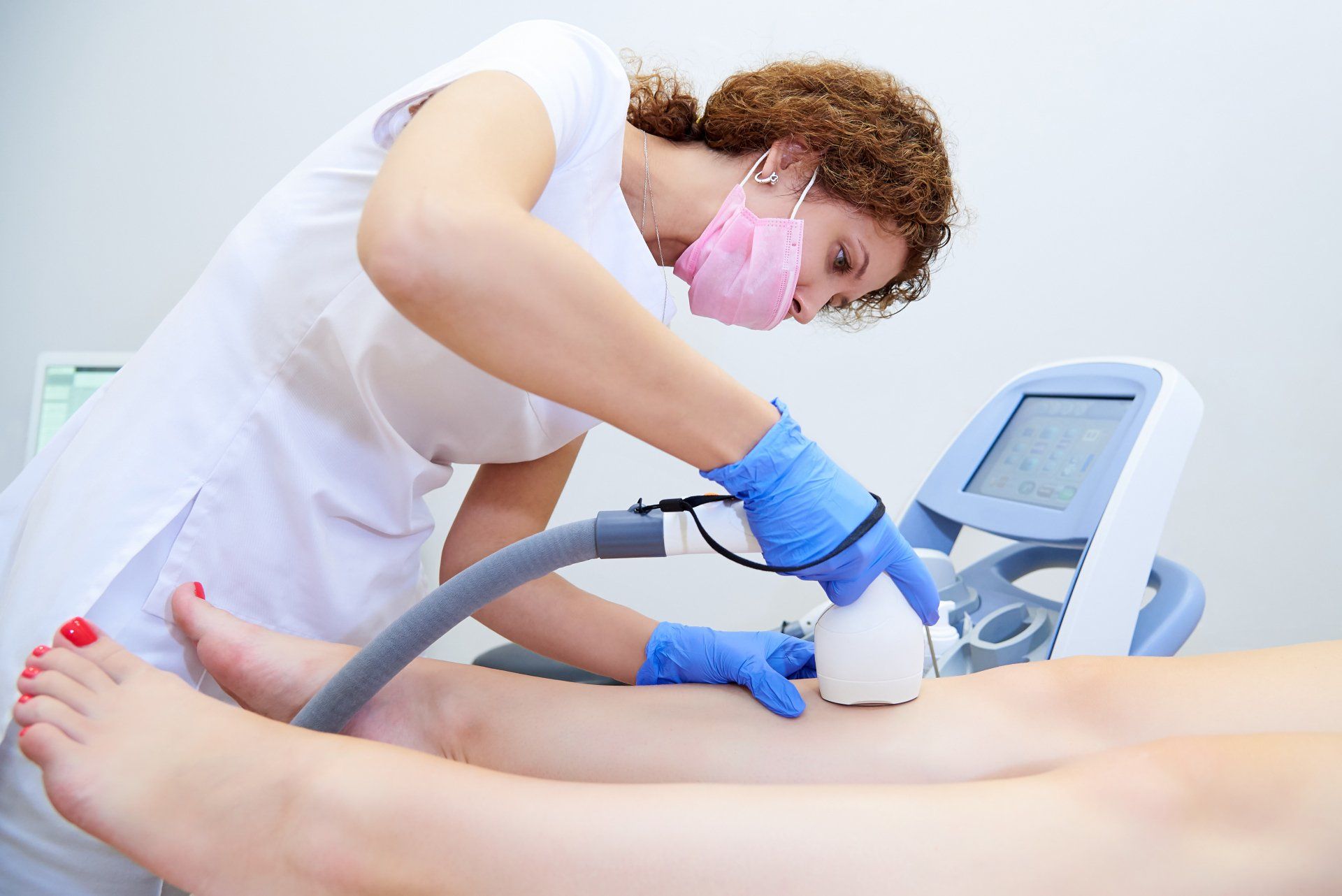 Aesthetic technician using a handheld device on a client’s leg in a bright clinic room