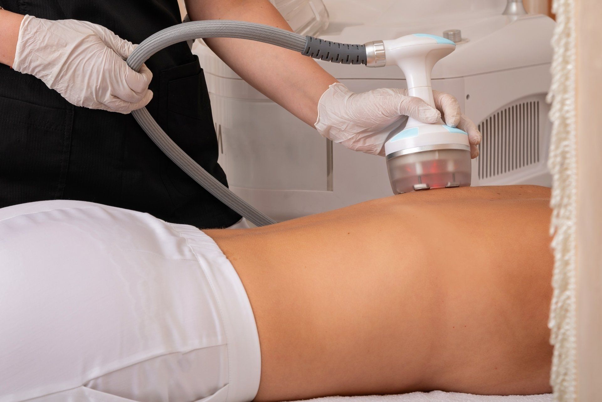Aesthetic body treatment with a handheld device on a client’s leg, wearing gloves in a spa setting