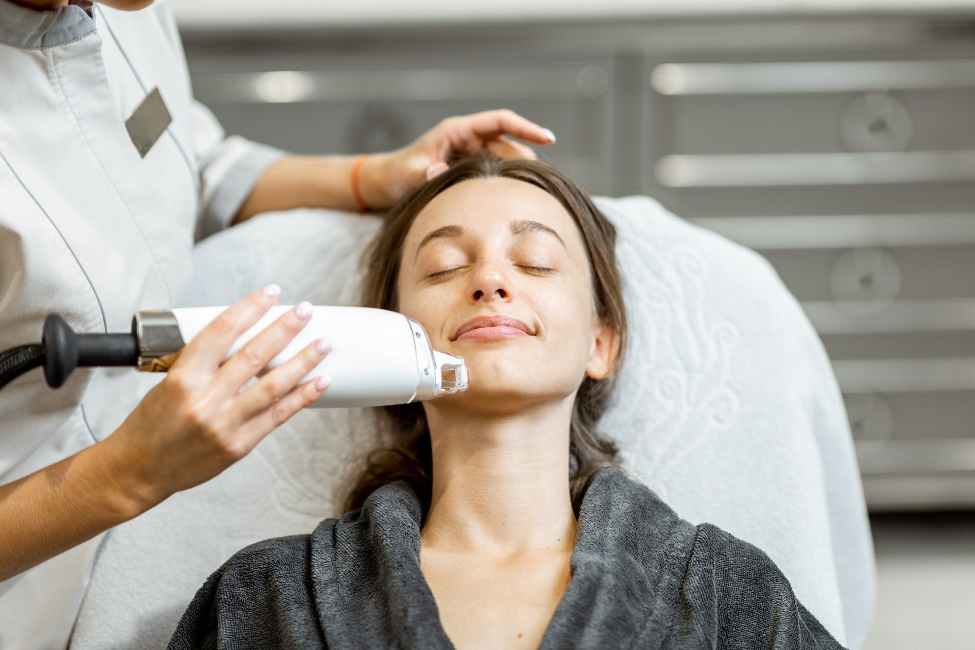 Facial treatment being applied with a handheld device as a client reclines with eyes closed