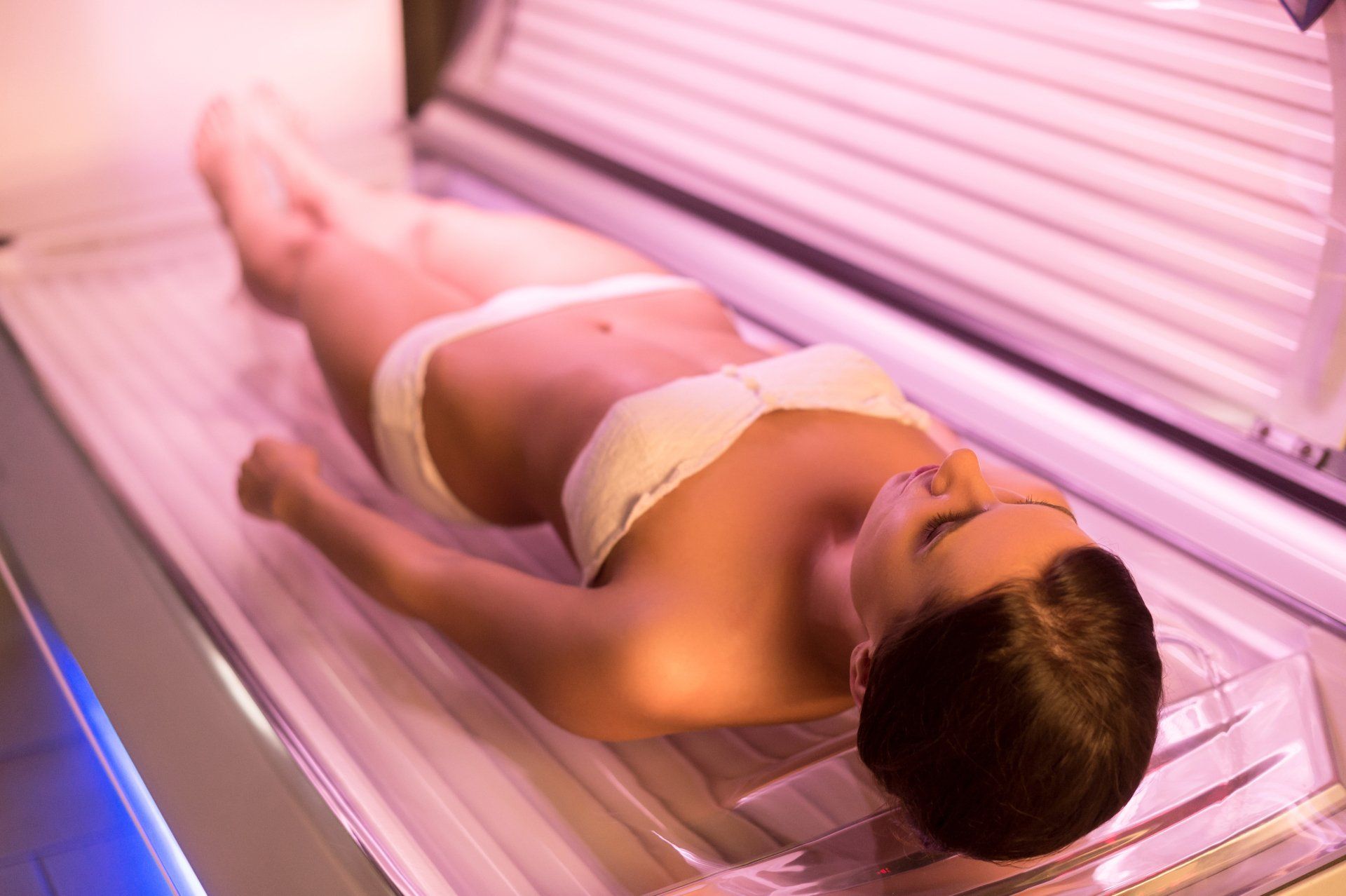 Person lying in a tanning bed under pink UV lights