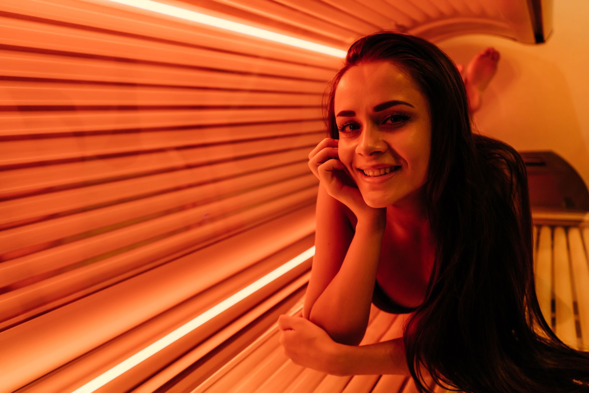 Smiling woman resting in a warmly lit tanning bed with orange glow and closed sunbed lid