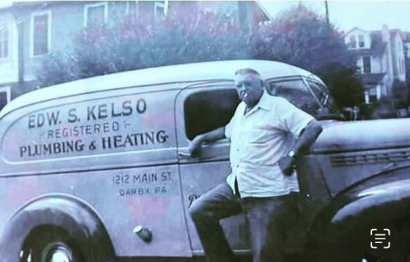 Man in work clothes leaning against a plumbing van.