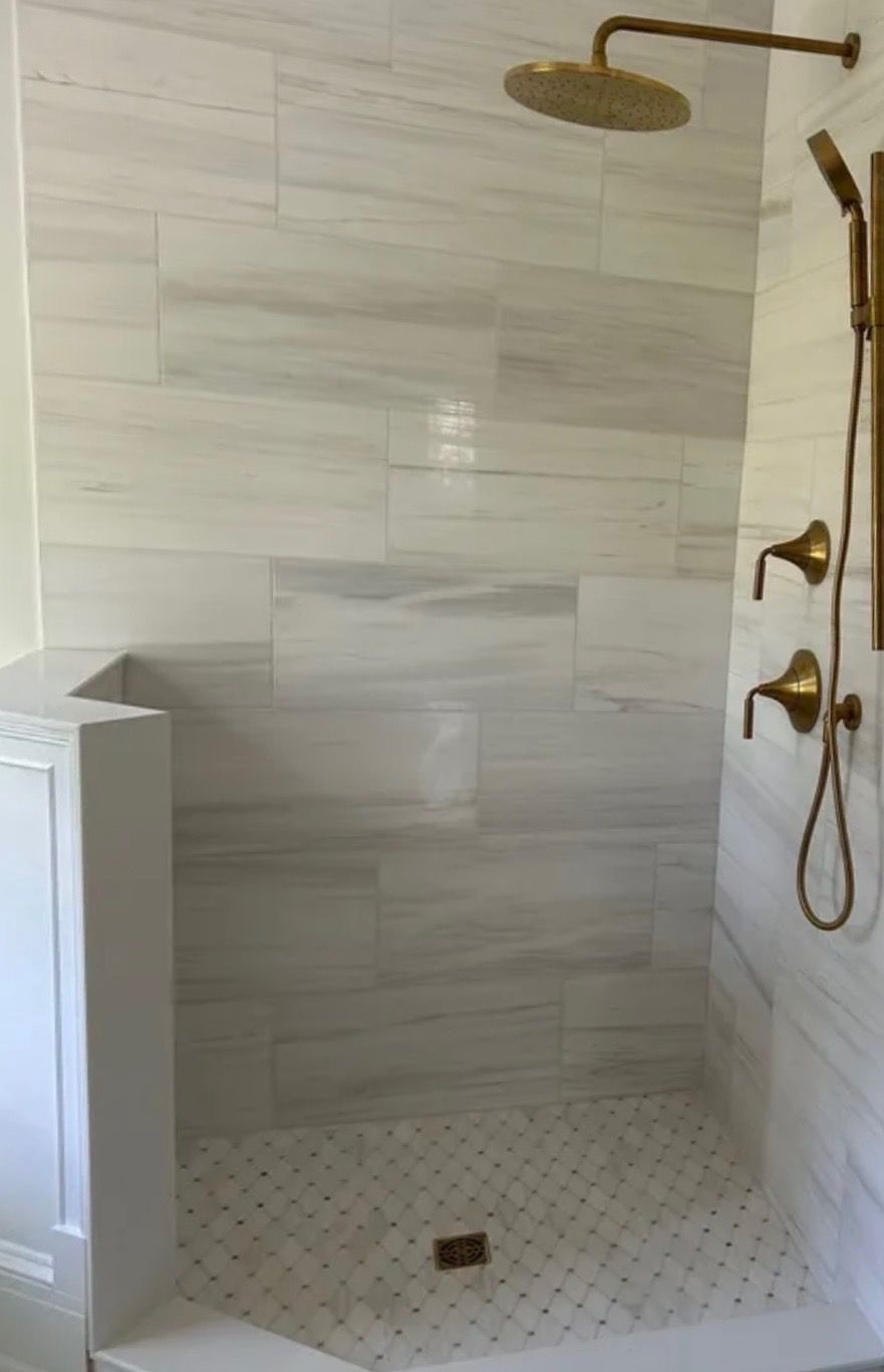 Walk-in shower with white tile walls, hex floor, and gold rainfall and handheld shower fixtures